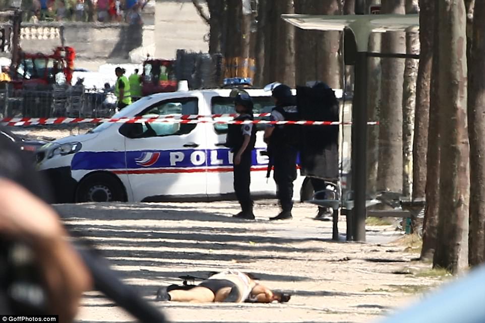 Police standing by as the perpetrator lies face down in the dusty sidewalk after having his clothes ripped from him